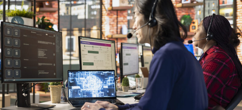 Team of multiethnic call center workers at office desk using AI to generate call scripts during conversation with customers. Multiracial customer support employees using AI to summarize clients issues